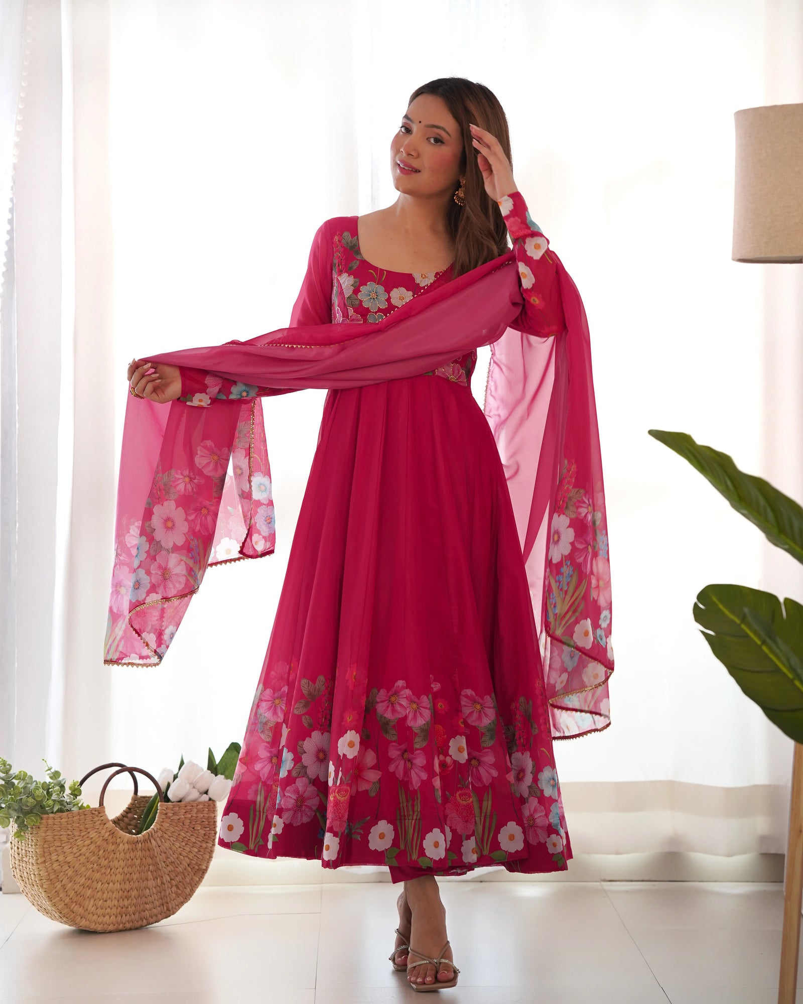 Woman in a pink floral dress with a matching scarf in a bright room.