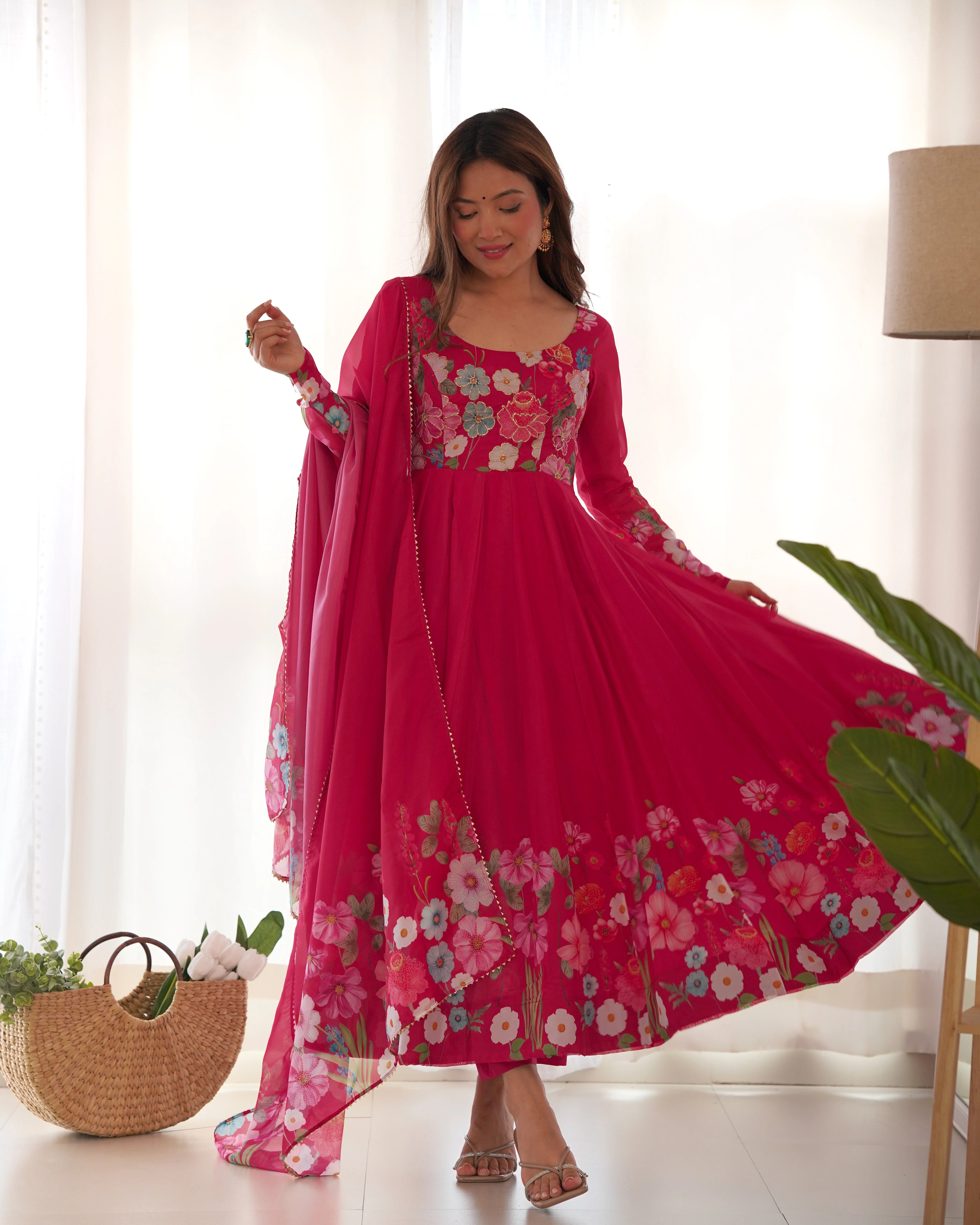 Woman wearing a pink floral dress with a matching dupatta in a bright room.