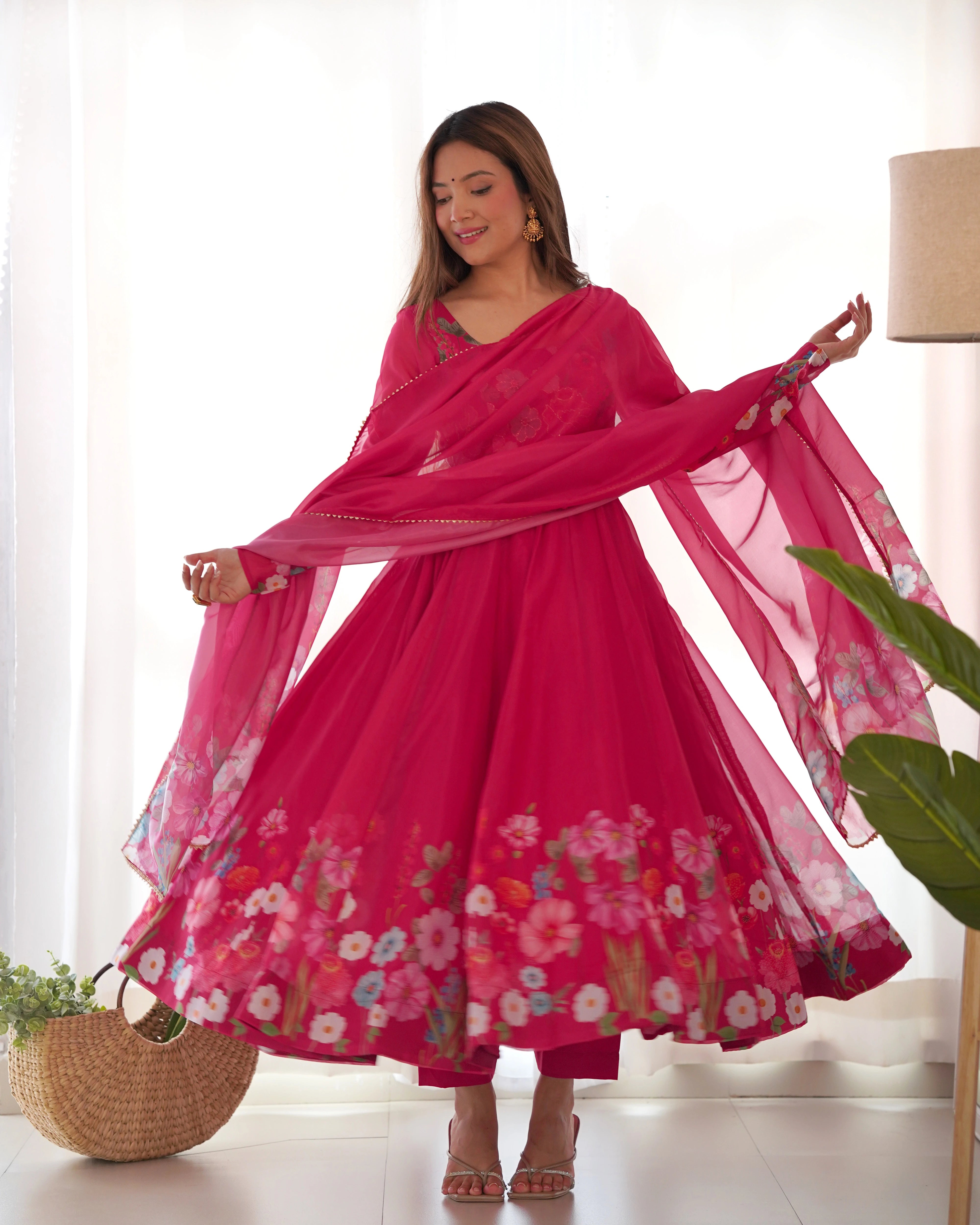 Woman in a pink floral dress with a matching dupatta in a bright room.