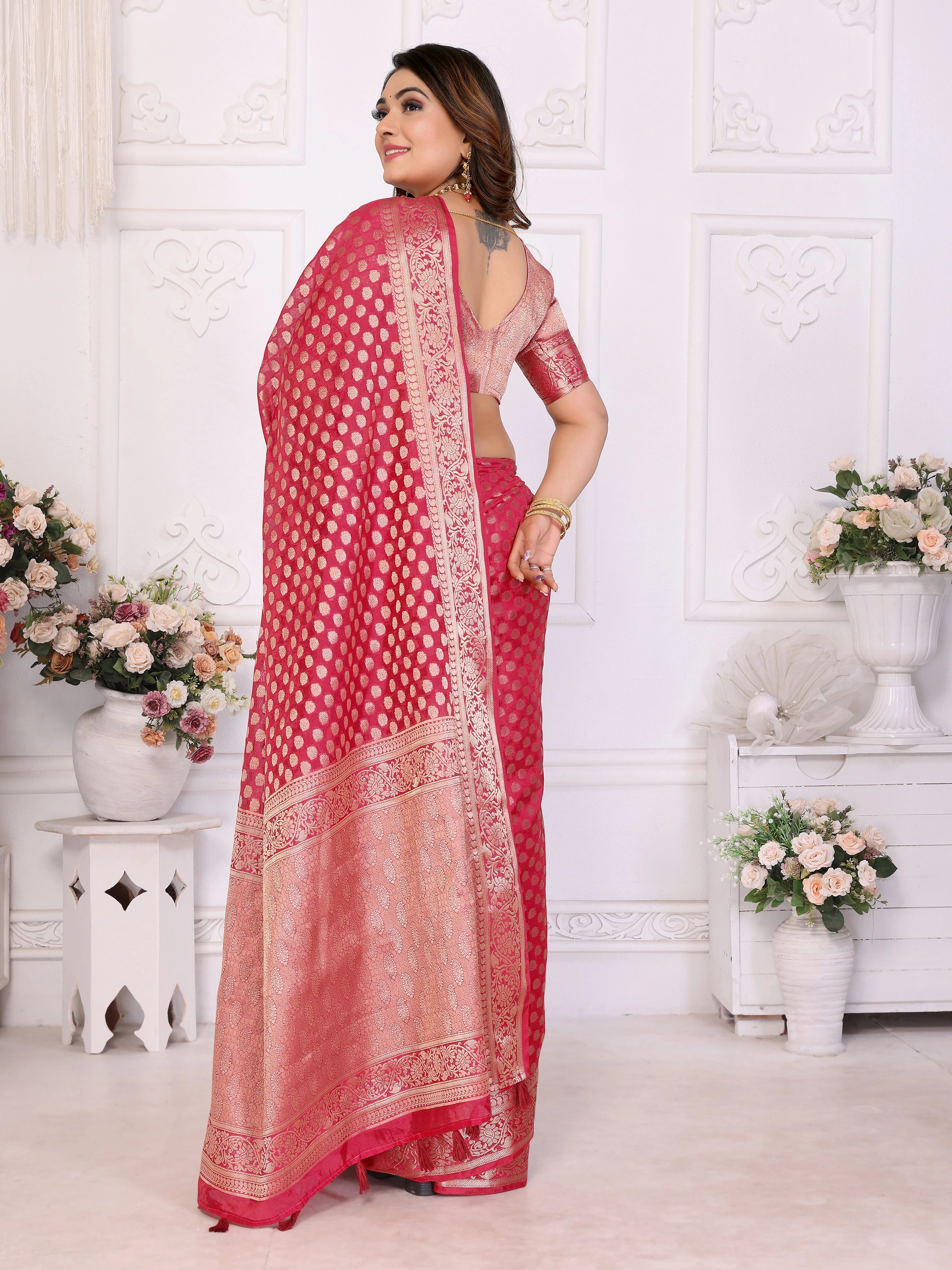 Woman wearing a red saree with white patterns in a decorated room.