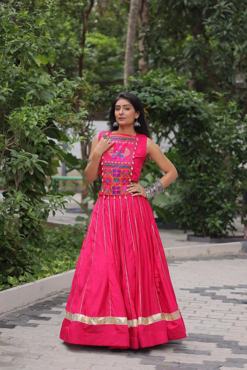 Woman in a bright pink traditional outfit with intricate designs standing outdoors.
