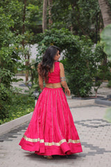 Woman in a bright pink traditional outfit walking outdoors with greenery in the background