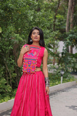 Woman in a bright pink traditional outfit with colorful embroidery standing outdoors.