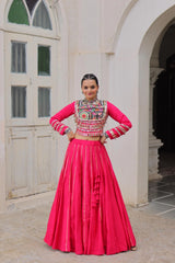 Woman in a traditional outfit with a pink top and red skirt standing in front of a white archway.