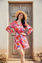 Woman in a colorful floral dress and straw hat standing in front of a wooden door.
