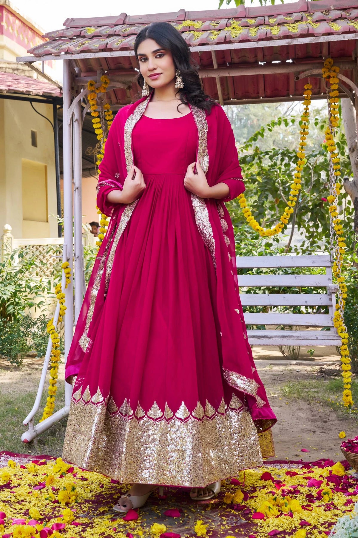 Woman in a red and gold traditional outfit standing in a decorated outdoor setting.