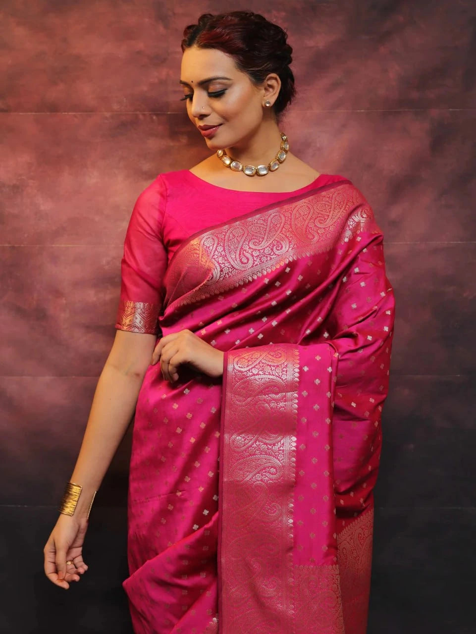 Woman wearing a pink saree with a metallic border against a dark background
