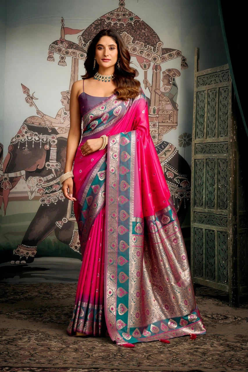 Woman in a pink saree with intricate patterns standing in front of an ornate wall.