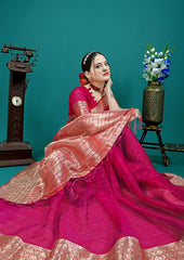 Woman in a pink saree with gold border sitting against a teal background