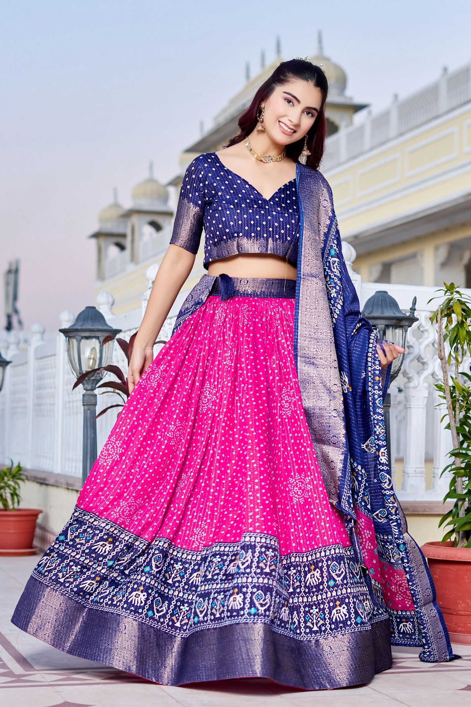 Woman in a traditional pink and blue outfit standing outdoors with architectural elements in the background