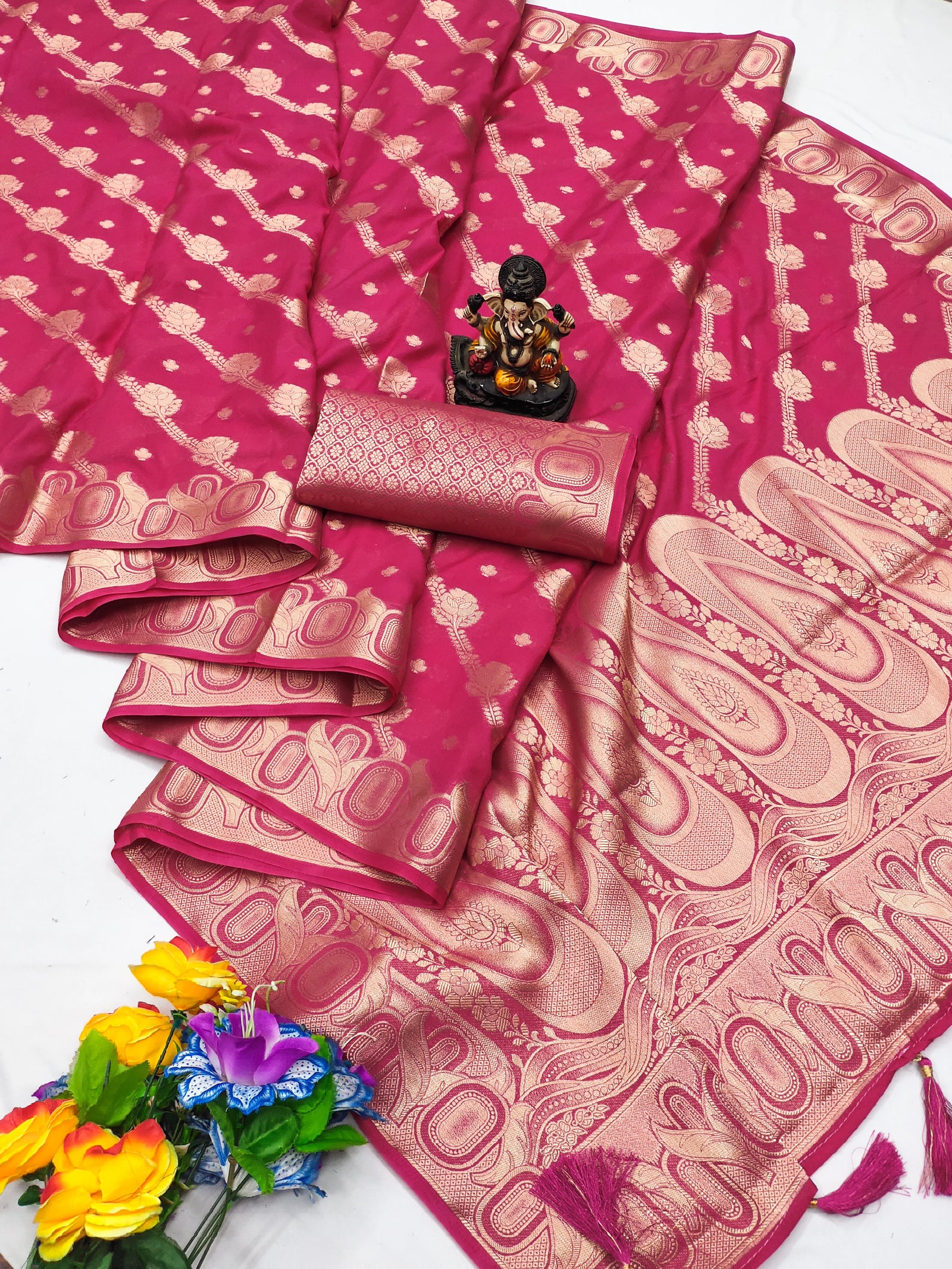 Pink saree with gold patterns, flowers, and a small statue on a white background