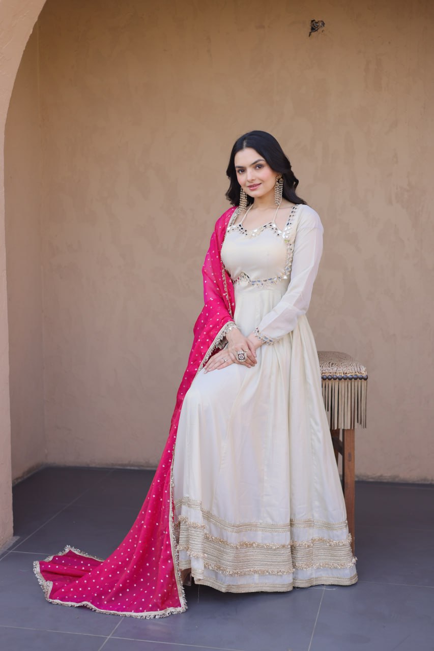 Woman in a white and pink traditional outfit standing against a beige wall.