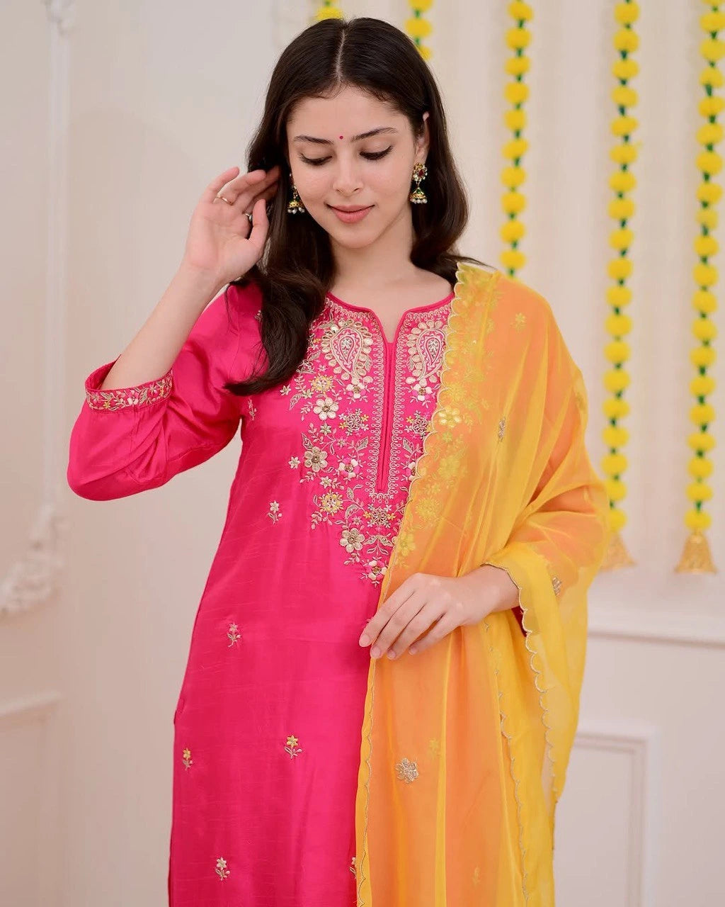 Woman wearing a pink embroidered kurta with a yellow dupatta against a neutral background