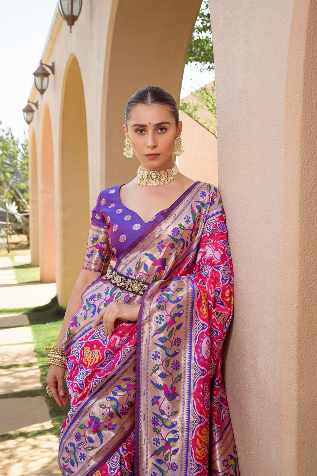 Woman in a colorful saree standing outdoors with architectural elements in the background