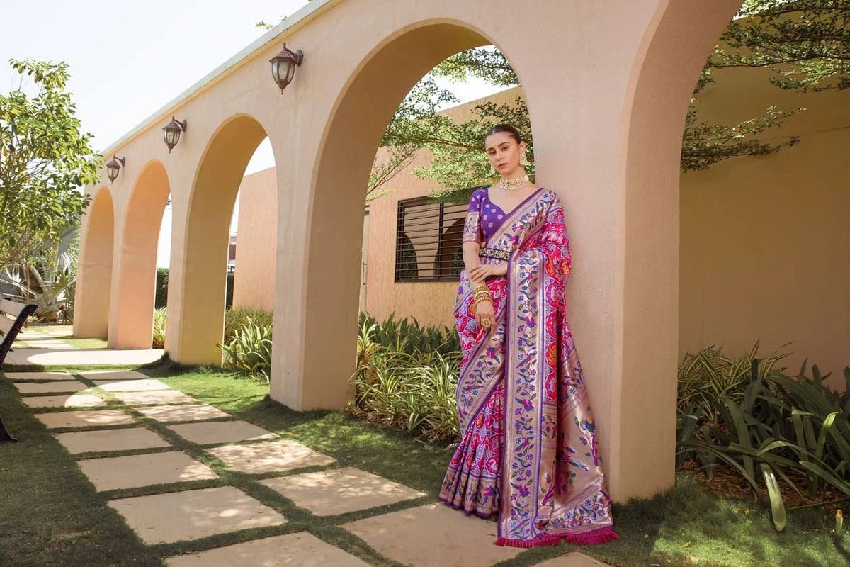 Woman in a colorful saree standing under an archway with greenery around
