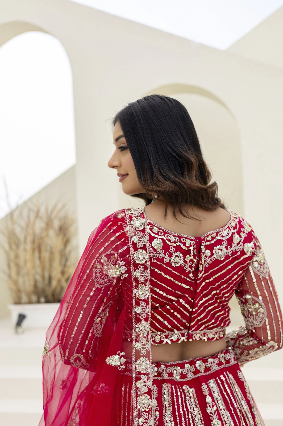 Woman wearing a red traditional outfit with intricate gold embroidery in an outdoor setting.
