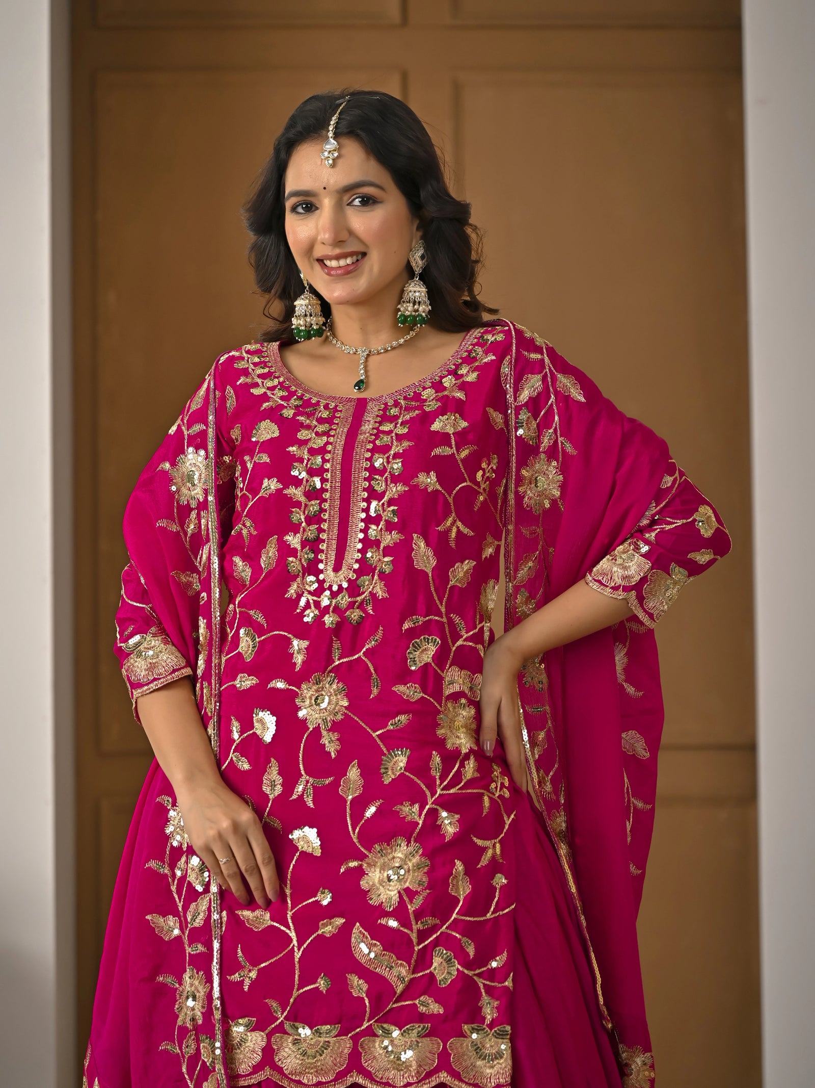 Woman wearing a pink embroidered traditional outfit with gold details against a plain background