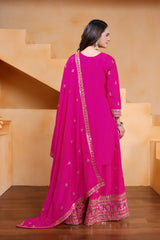 Woman wearing a bright pink traditional outfit with gold embroidery in a neutral setting.