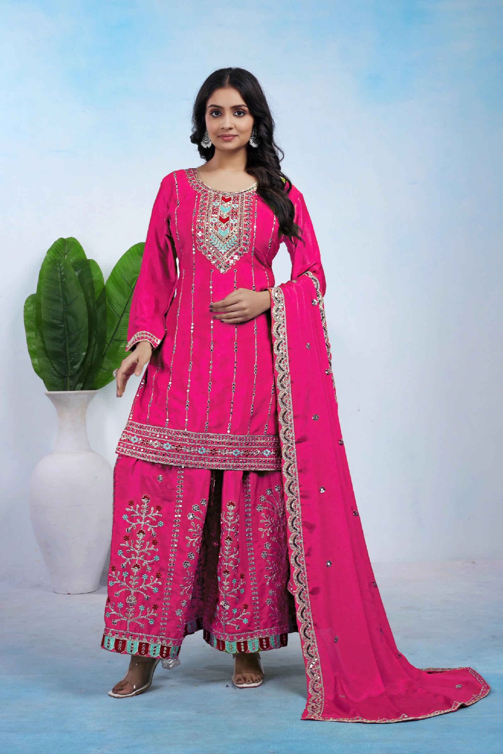 Woman wearing a pink traditional outfit with intricate embroidery against a light blue background.