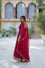 Full-length back view of a woman in a flowing magenta gown. The dress has a deep round back with tie-up detailing. She drapes a matching sheer dupatta over her shoulder in a tiled courtyard with traditional arches.