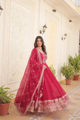 Woman in a pink traditional outfit standing in a decorated room with plants.