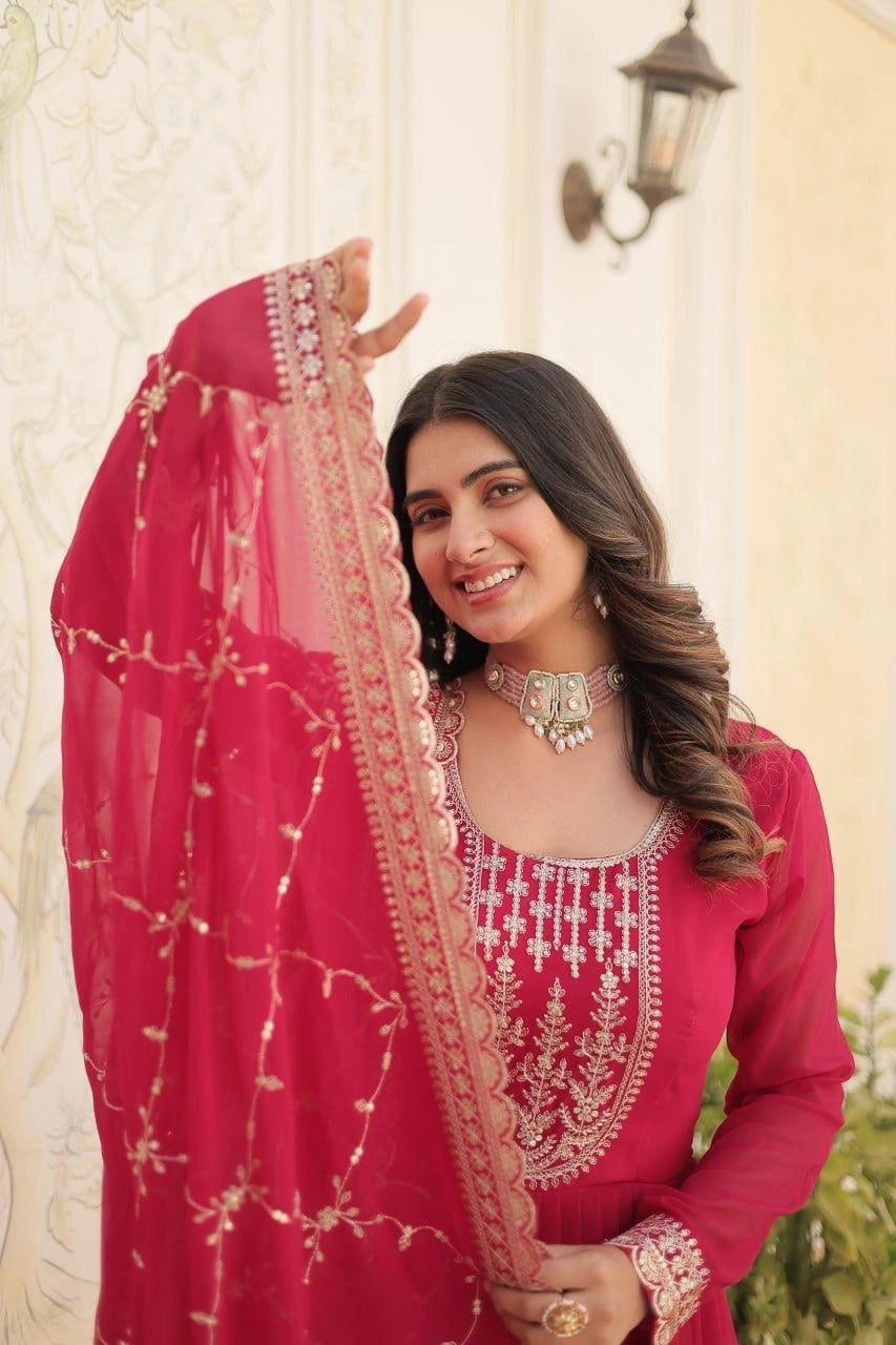 Woman in a pink embroidered outfit with a decorative headscarf, standing outdoors.