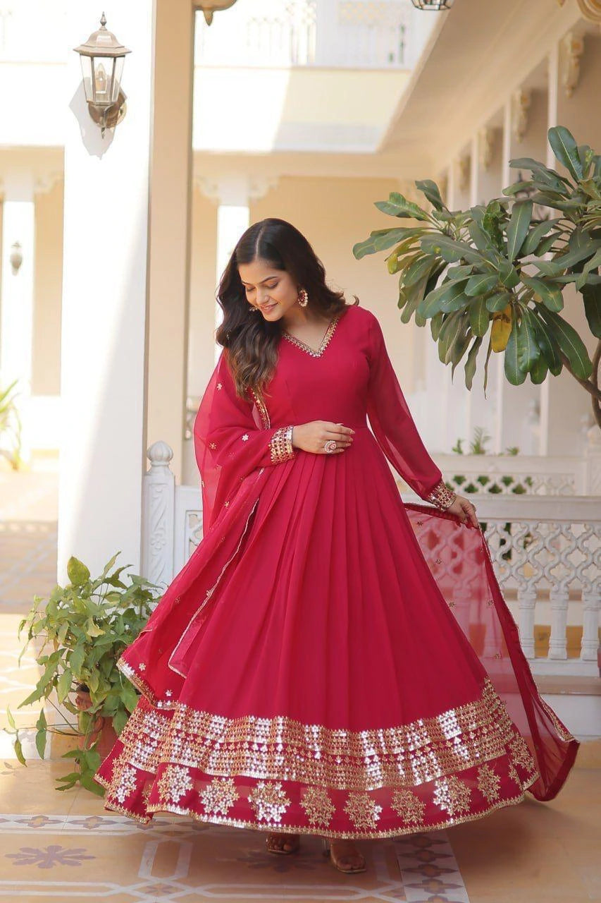 Woman in a red traditional outfit with gold details standing in a decorated indoor setting.