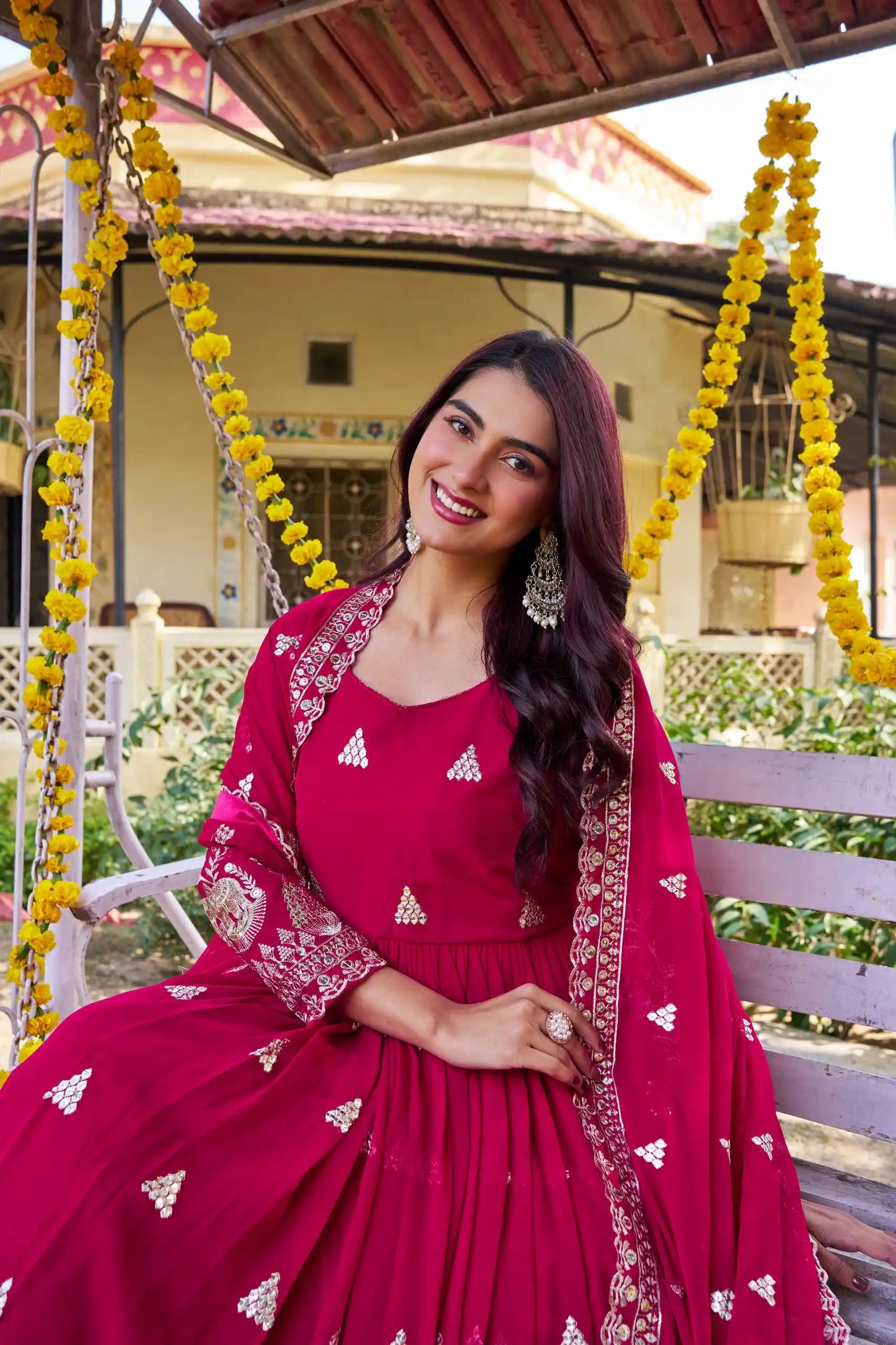 Woman in a red traditional outfit sitting on a swing with floral decorations.