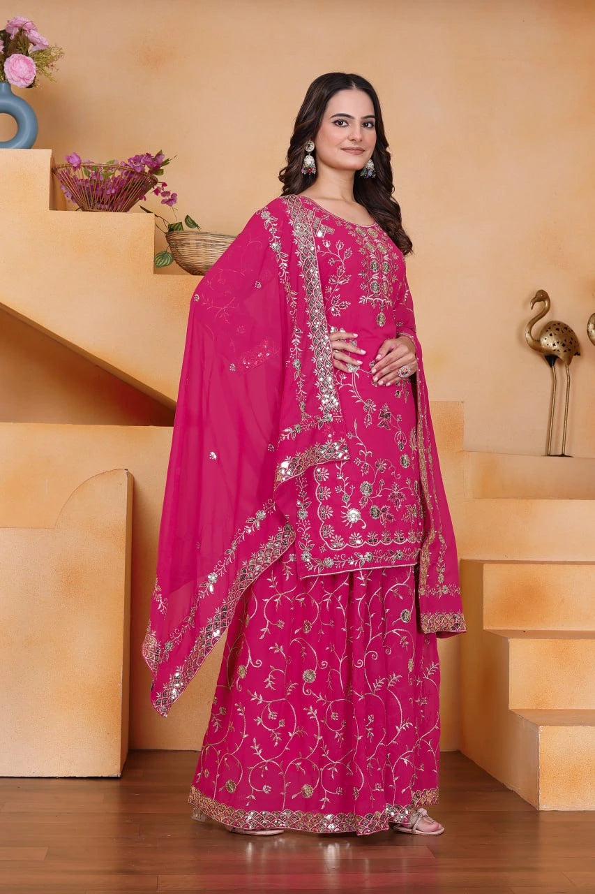 Woman in a pink traditional outfit with intricate designs standing indoors.
