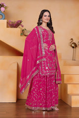 Woman in a pink traditional outfit with intricate designs standing indoors.
