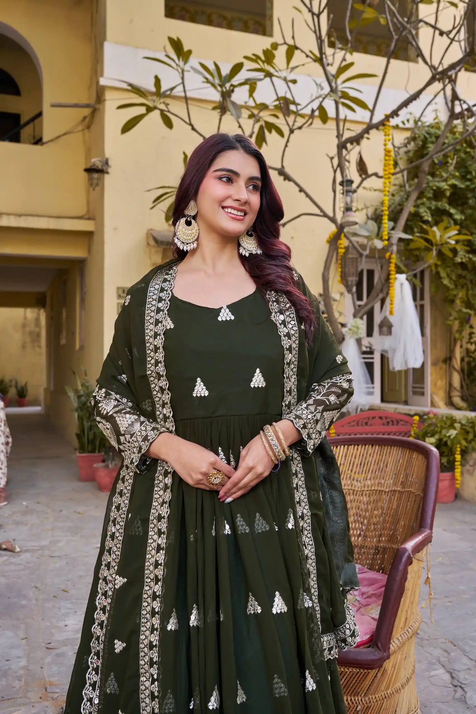 Woman in a dark green traditional outfit with white patterns standing outdoors.