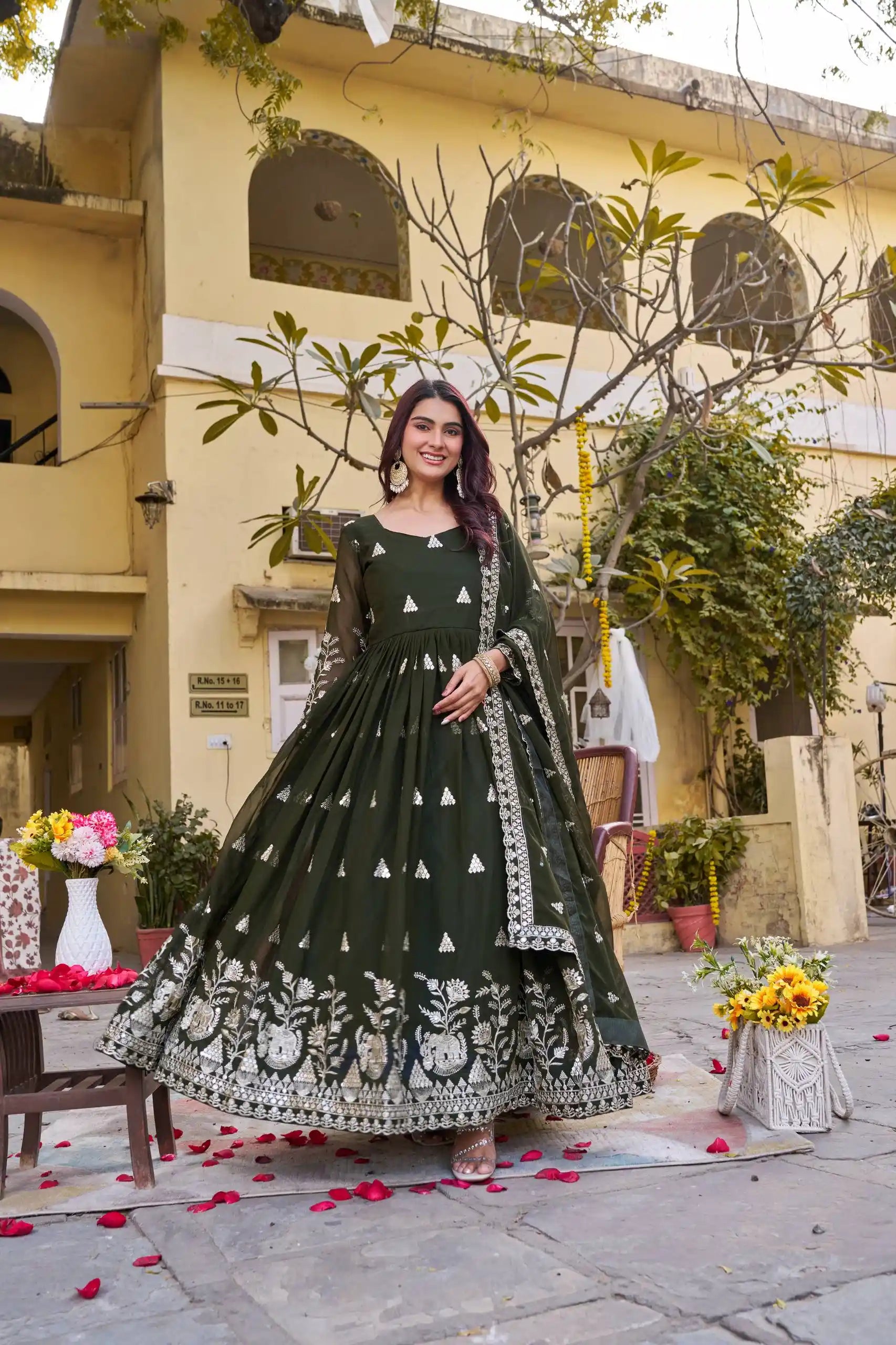 Woman in a dark green traditional outfit standing in front of a building with decorative elements.