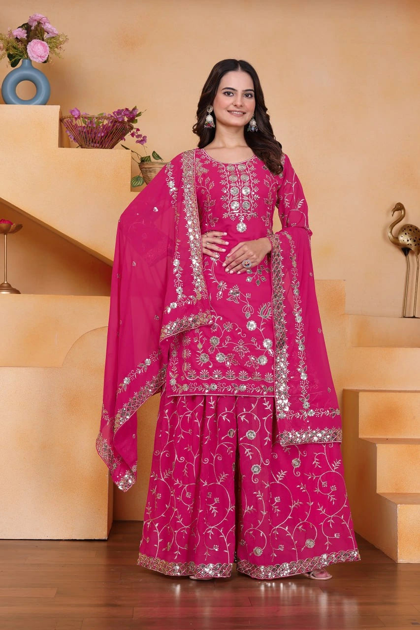 Woman wearing a pink traditional outfit with silver embroidery in a home setting.