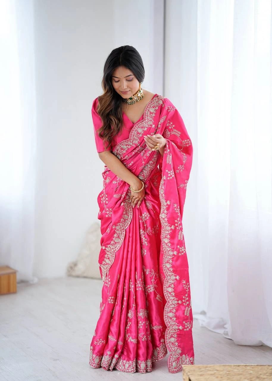 Woman wearing a bright pink saree with white patterns in a minimal indoor setting.