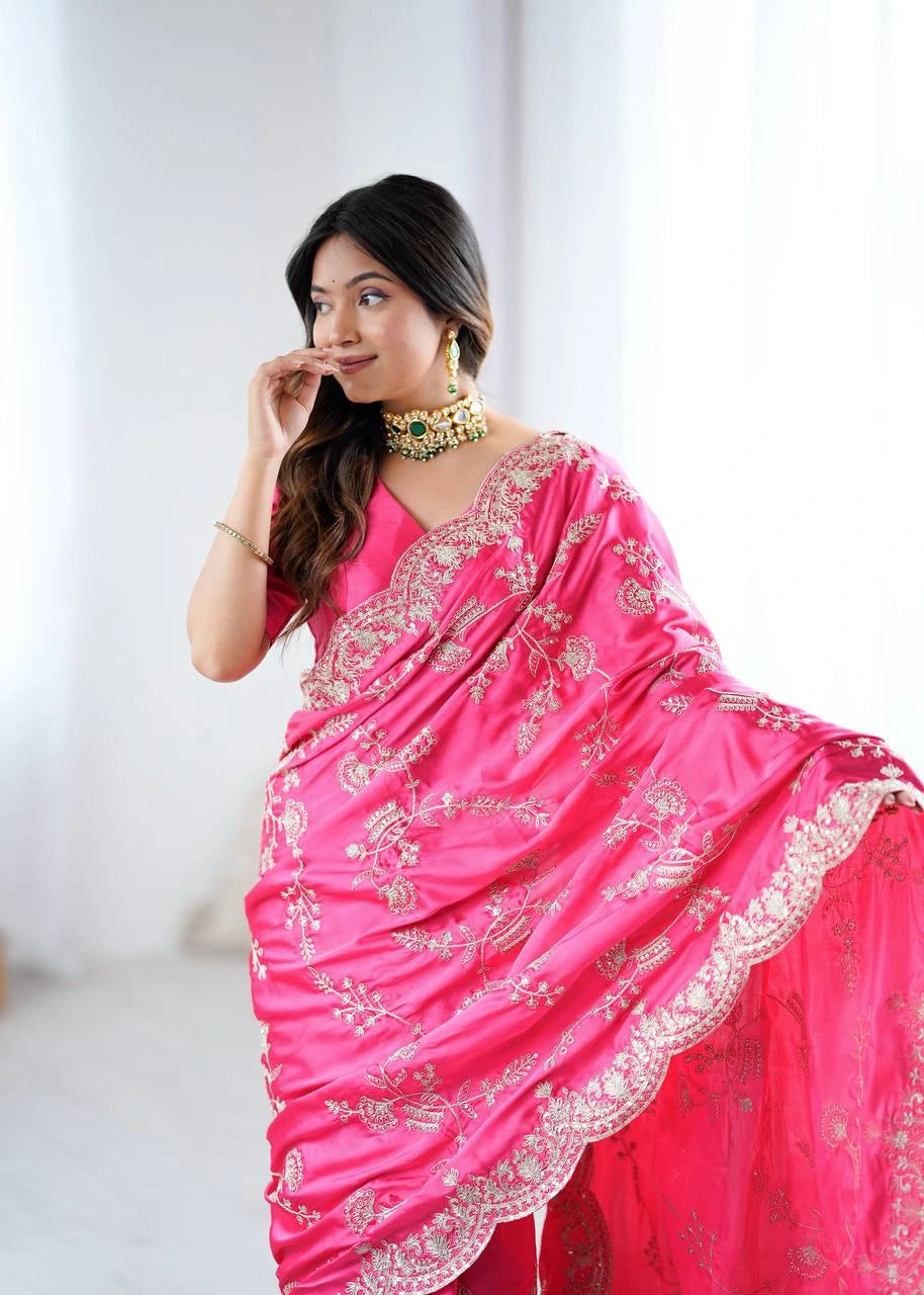 Woman wearing a bright pink saree with intricate designs on a plain background