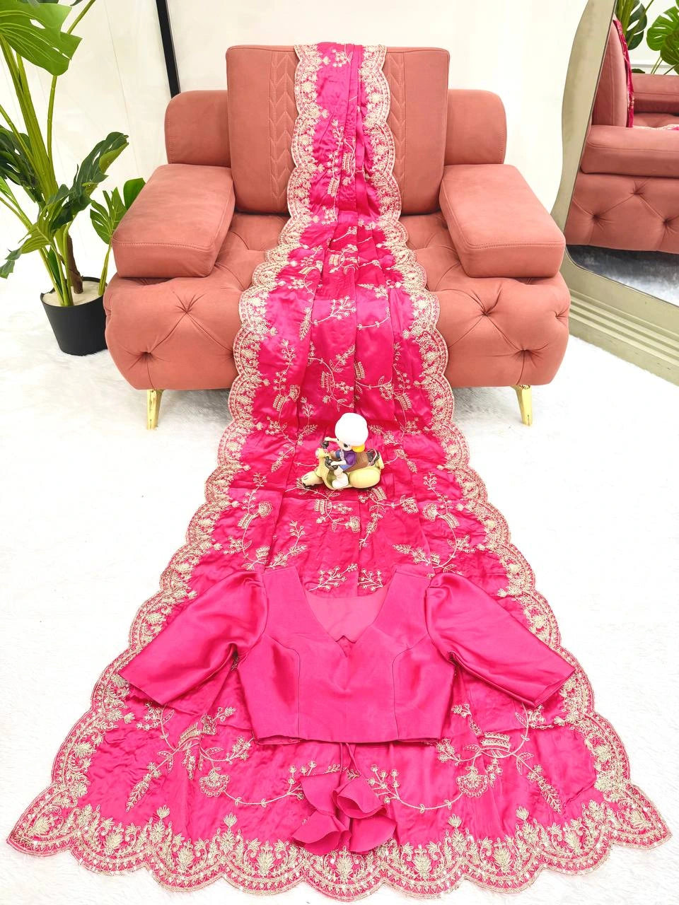 Pink embroidered garment on a pink sofa with a plant and mirror in the background