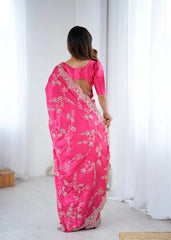 Woman wearing a bright pink saree with white floral patterns in a minimal indoor setting.