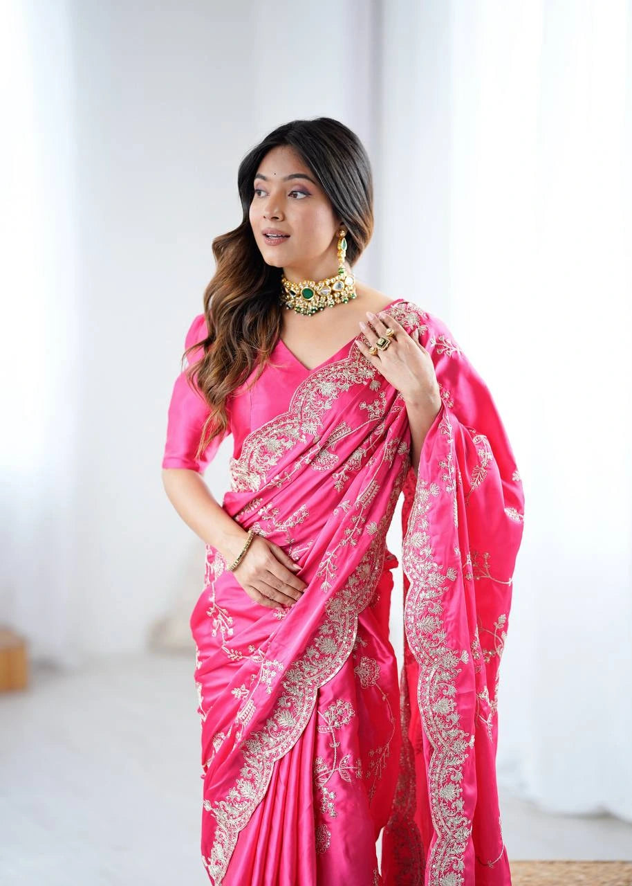 Woman wearing a bright pink saree with white embroidery against a plain background