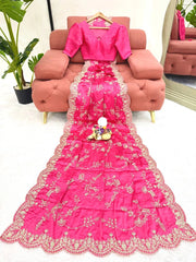Pink embroidered saree with a hanger on a pink sofa in a room setting.