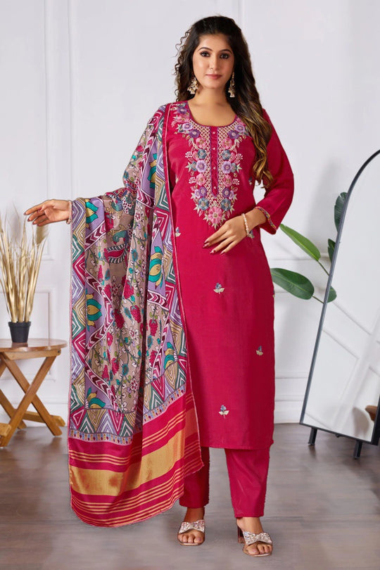Woman wearing a pink embroidered outfit with a colorful scarf indoors.