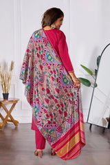Woman wearing a colorful traditional outfit with a patterned dupatta in a minimal indoor setting.