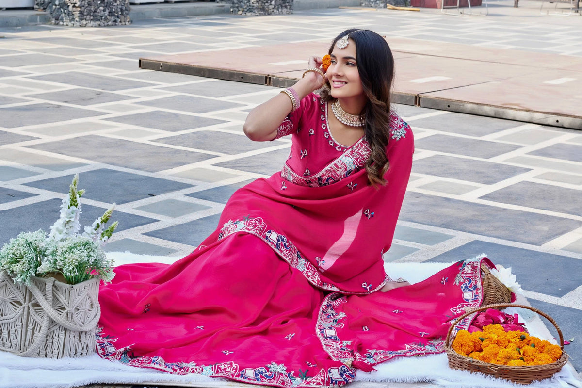 Woman in a bright pink saree with floral patterns sitting on a stone pavement.