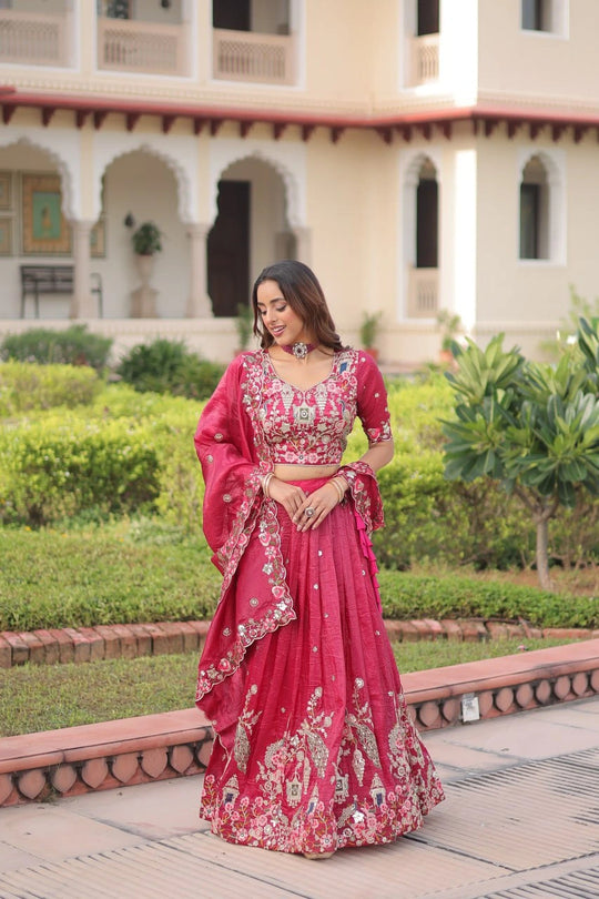 Woman in a pink traditional outfit standing in front of a building with greenery.