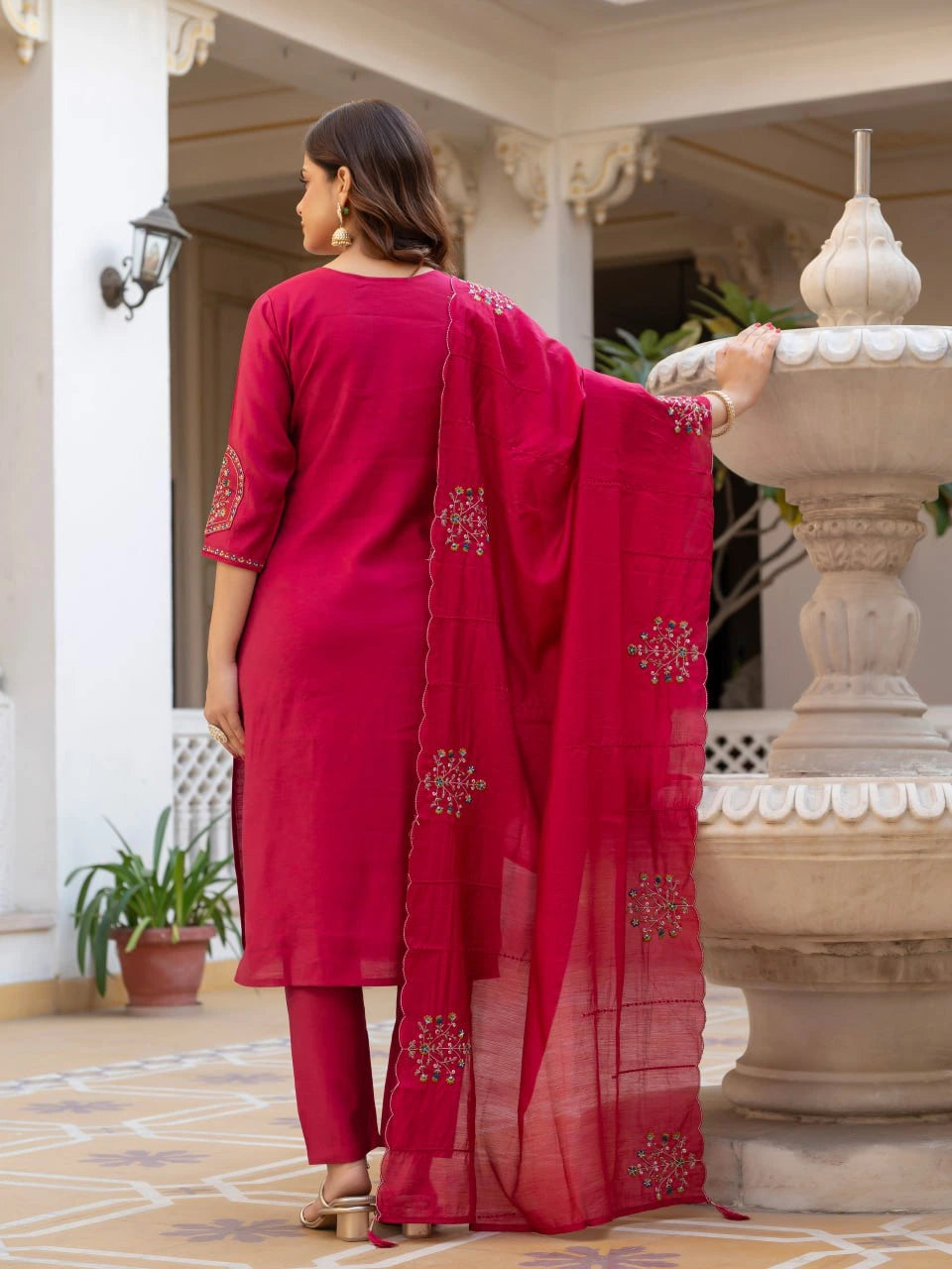 Woman in a red traditional outfit standing in front of a decorative fountain.