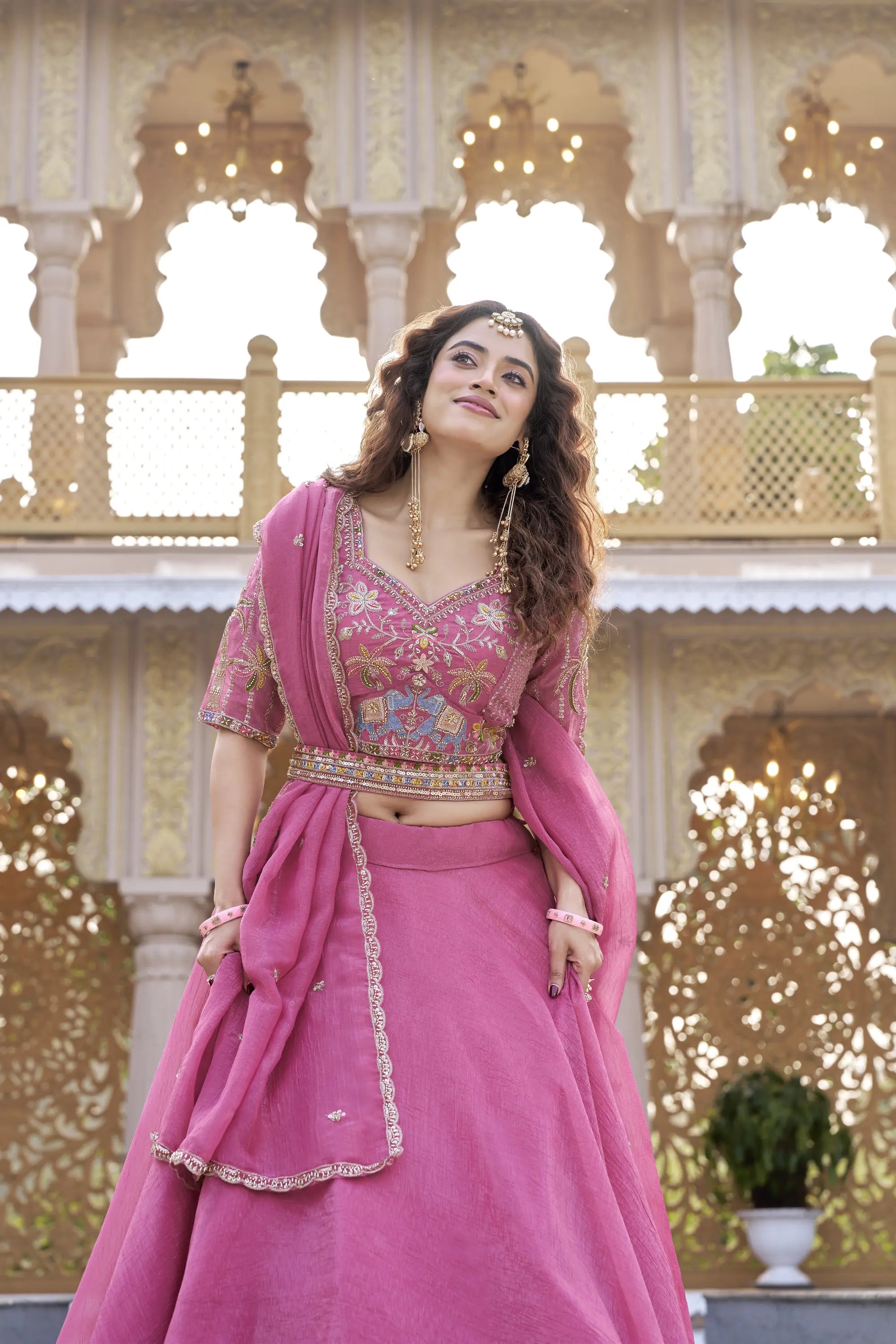 Woman in a pink traditional outfit standing in front of decorative architecture.