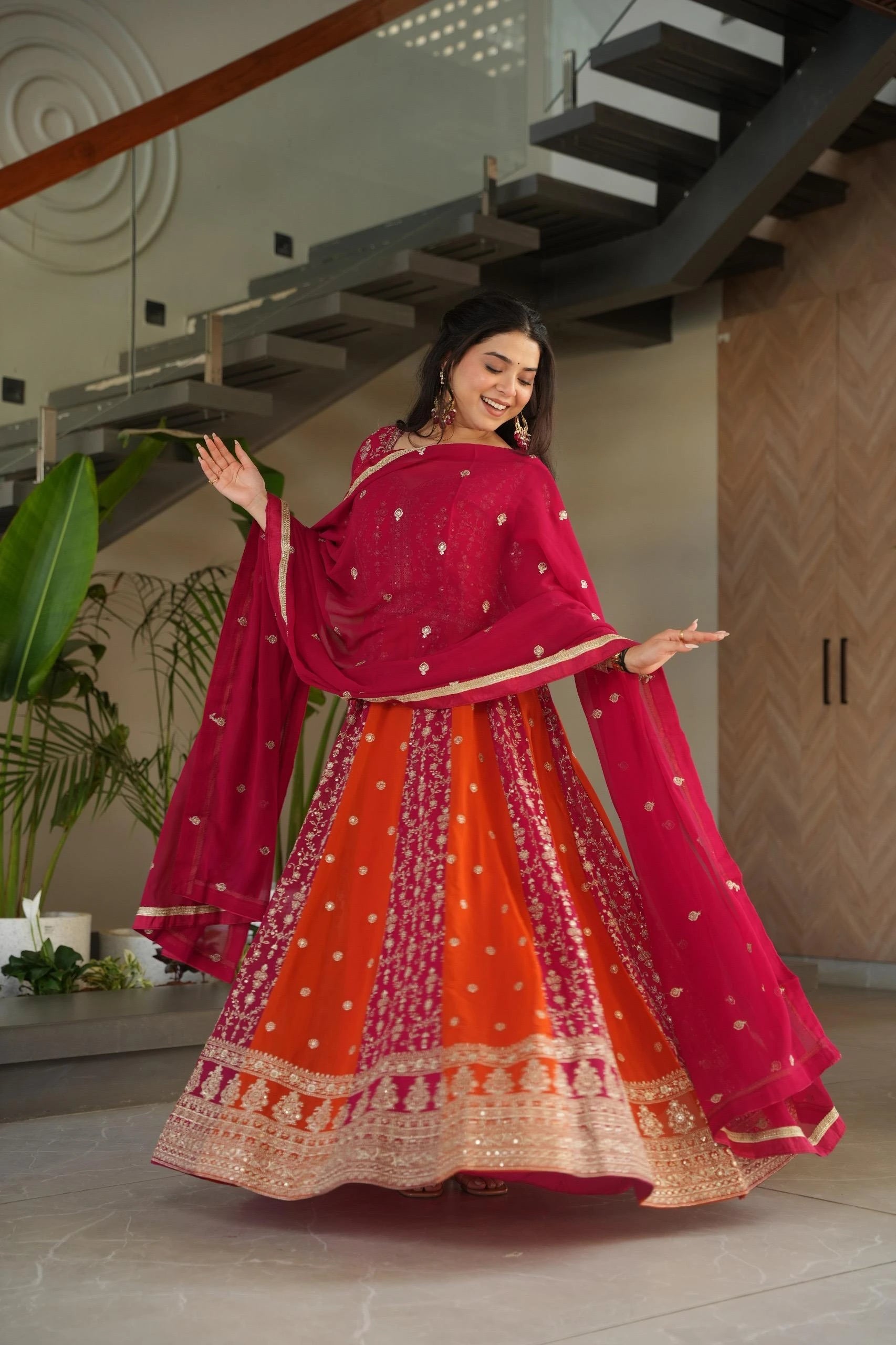Woman in a vibrant red and orange traditional outfit standing indoors.
