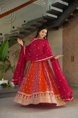 Woman in a vibrant red and orange traditional outfit standing indoors.