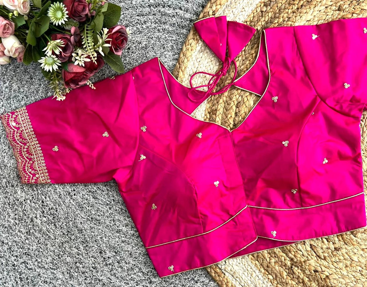 Pink blouse with intricate designs on a textured surface with flowers in the background