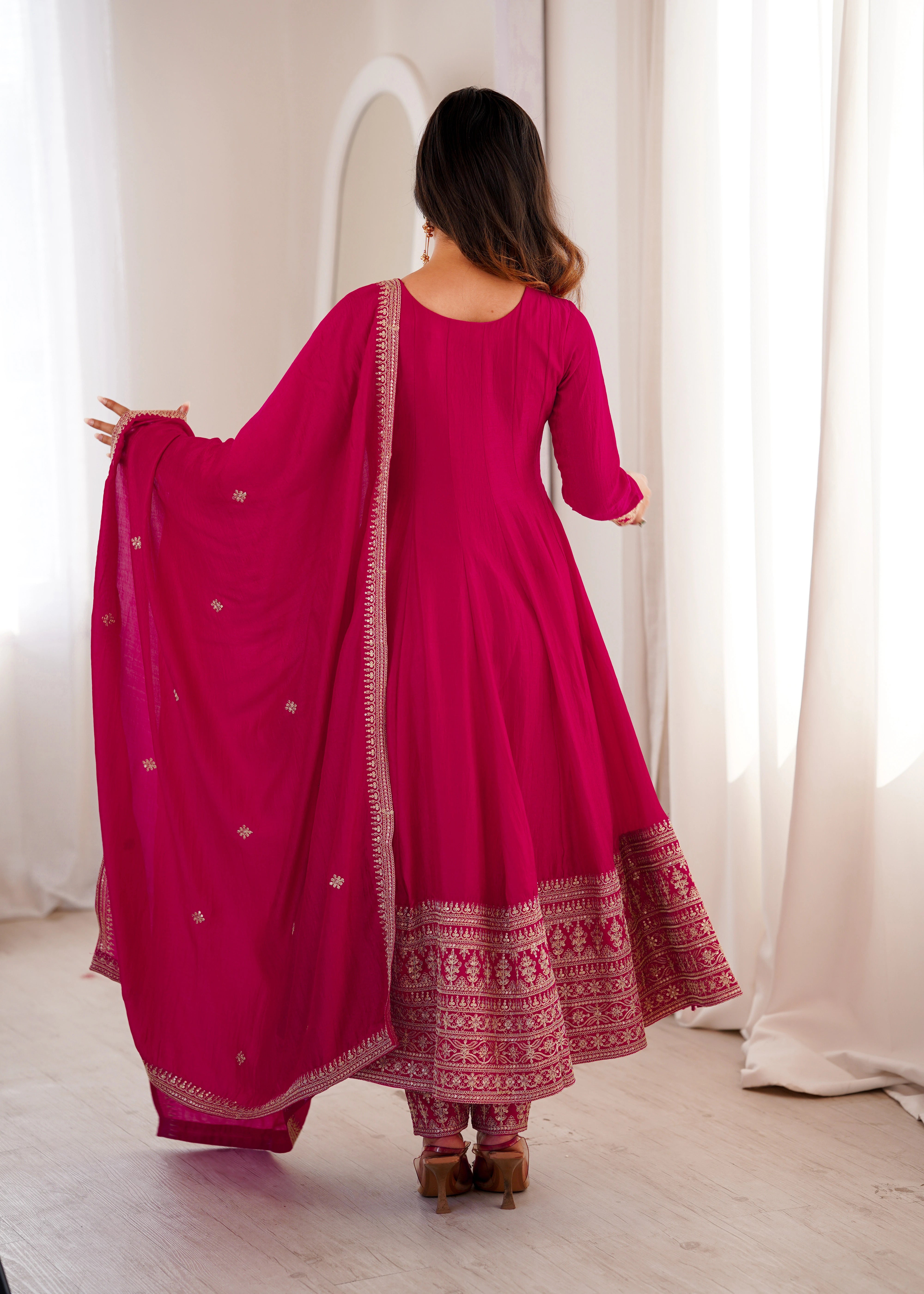 Woman wearing a pink traditional outfit with a matching dupatta in a bright room.