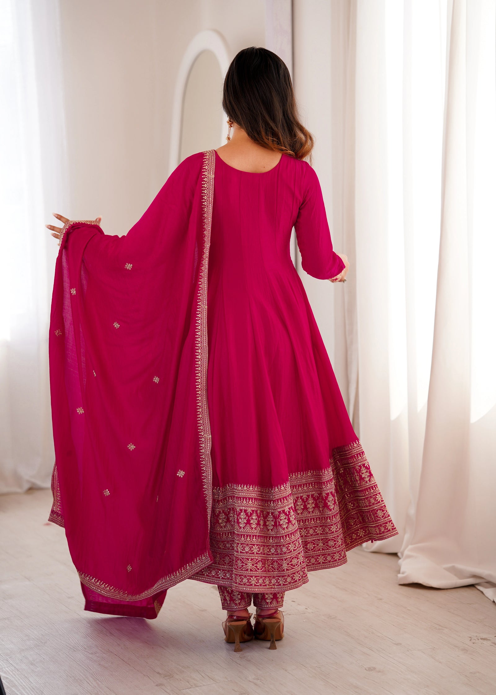 Woman wearing a pink traditional outfit with a matching dupatta in a bright room.